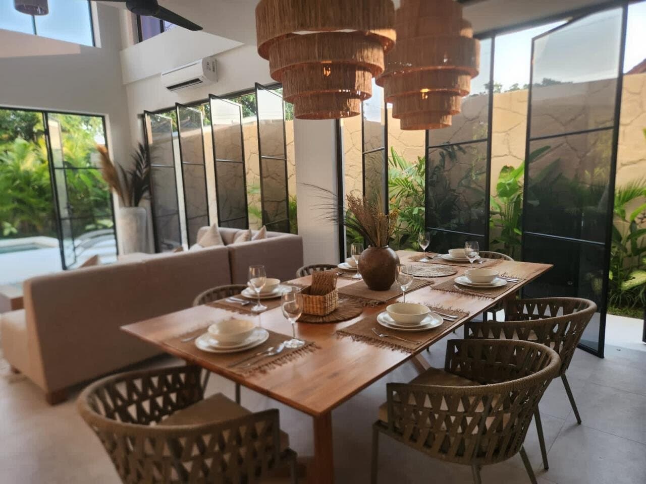 Oak dining table with woven chairs under a double-height steel window