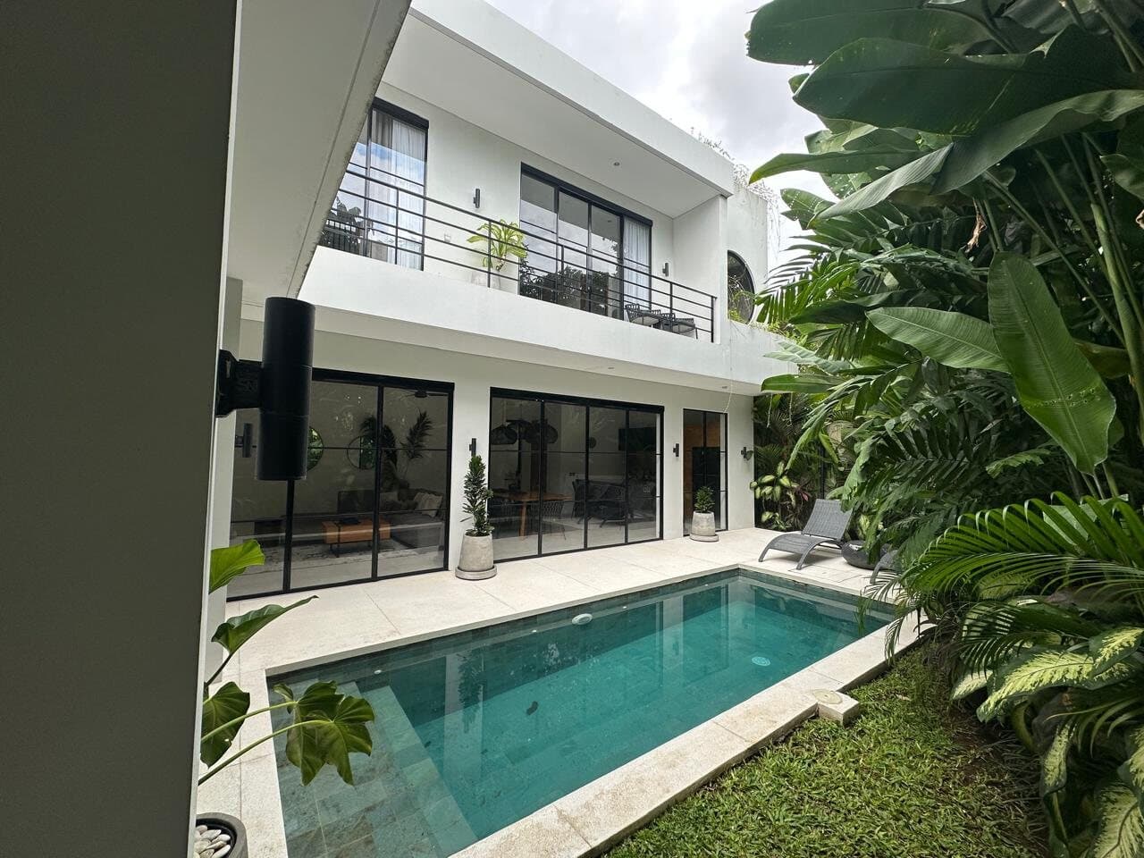 Two-storey white villa with black steel windows and a pool, from the garden